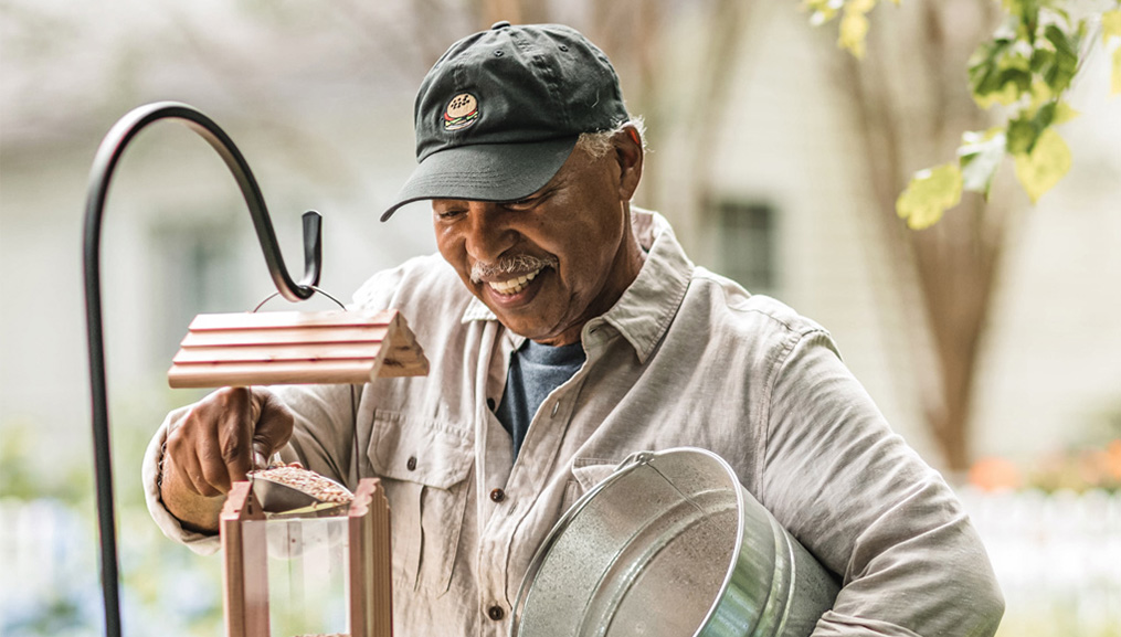 An older man refilling his bird feeder.