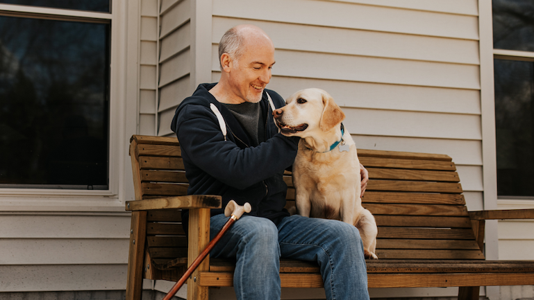 Man with a cane sitting on a bench smiling at his dog